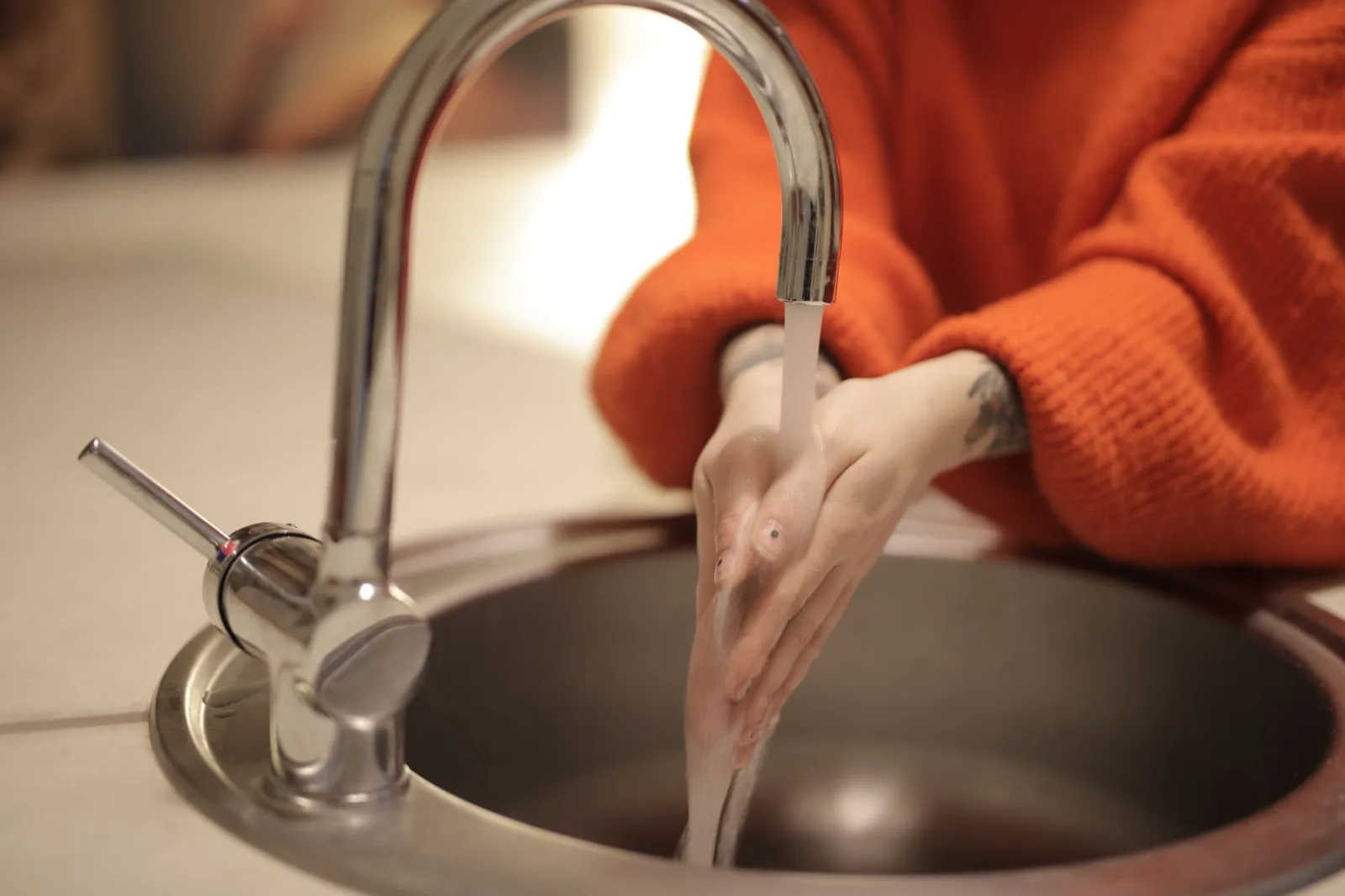 Person in an orange jumper washing their hands under a kitchen tap