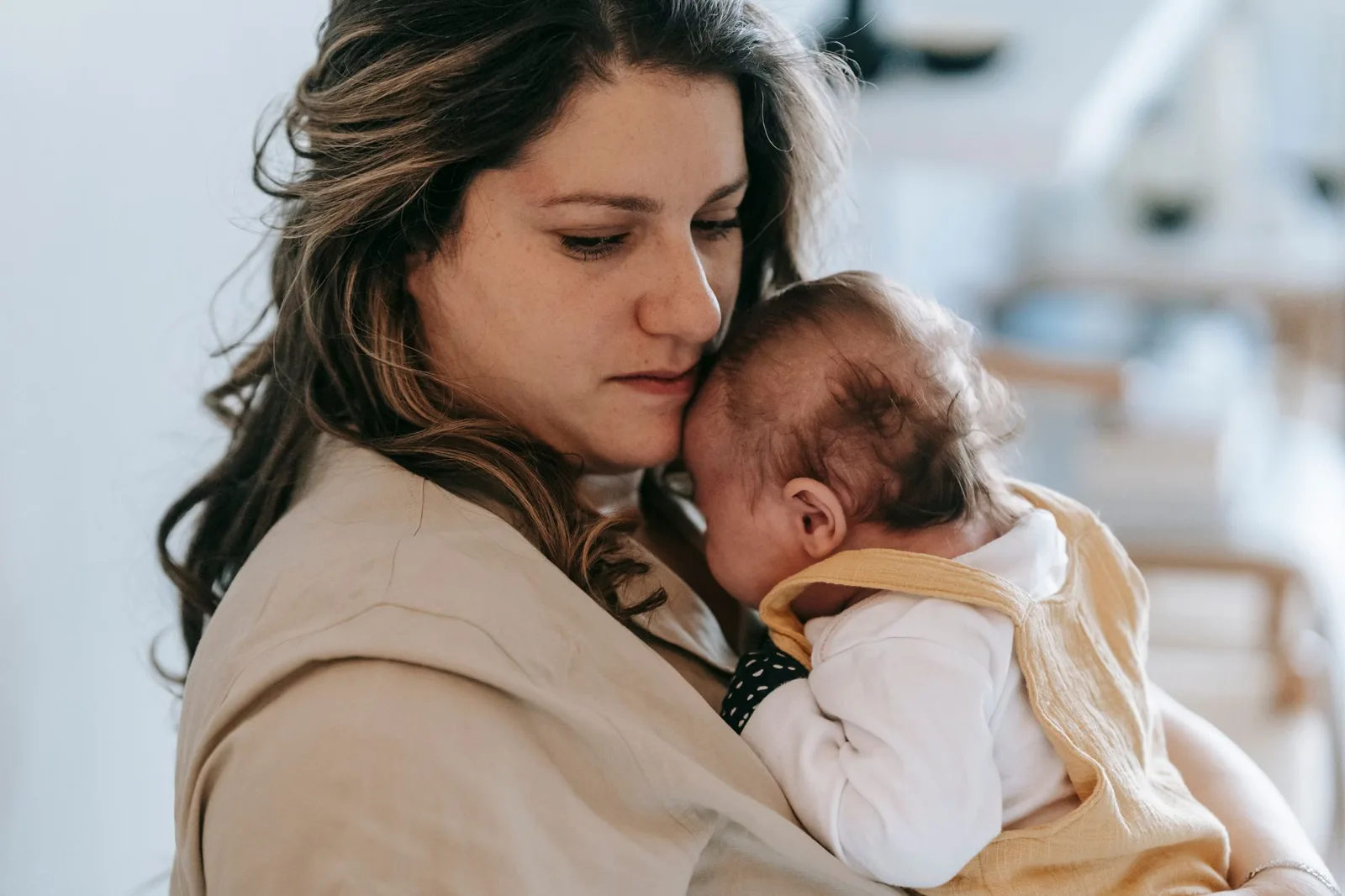 Mother holding her newborn baby close against her shoulder at home